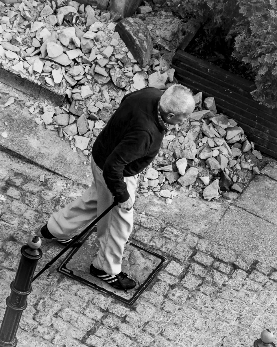 Older man dragging a shopping trolley past a pile of rubble